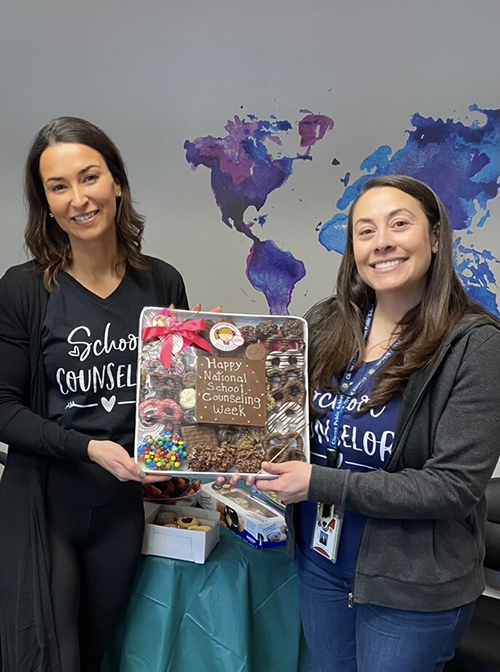 Mrs. Suzanne Lang and Ms. Dara Weiss holding up a tray of goodies